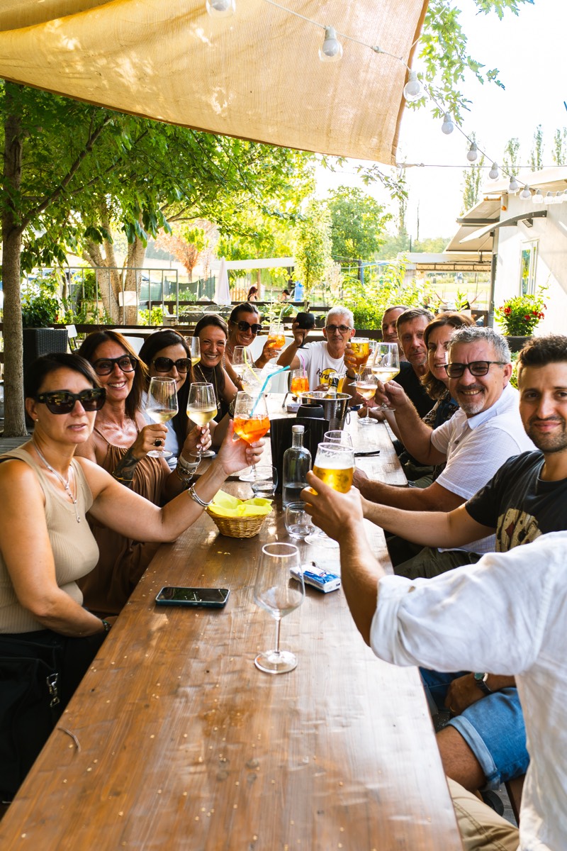 Una tavolata di amici brinda con lo spritz sotto le luci del pergolato